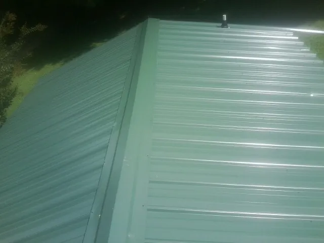 New green metal panels meeting at the ridge of a roof — Flat Roof Repair work by our crew in Lansing