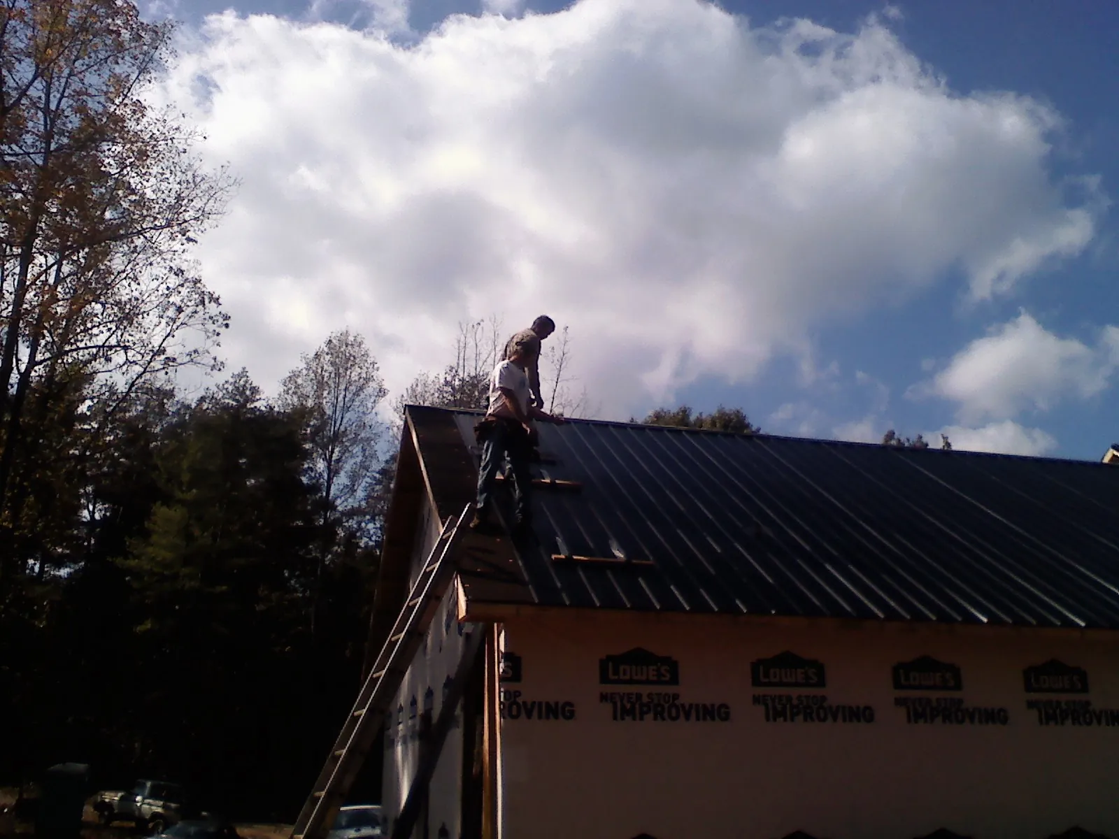 Roofer fastening dark metal panels high against a cloudy sky, from a Roof Inspection job in Lansing